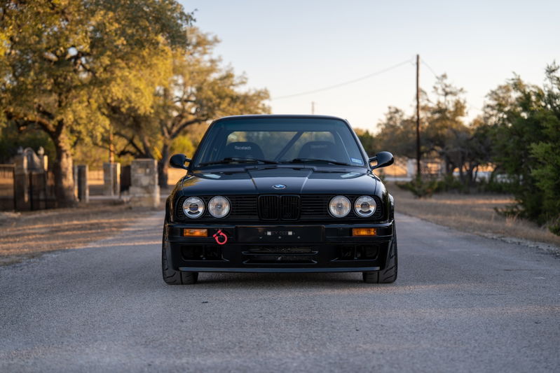 Front view of a black 1989 BMW 325is with racing seats and a tow hook.
