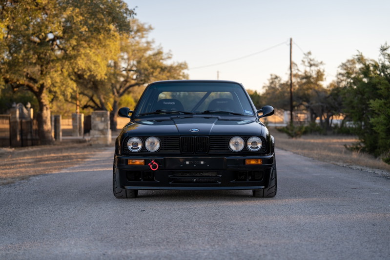 Front view of a black 1989 BMW 325is with racing seats and a tow hook.