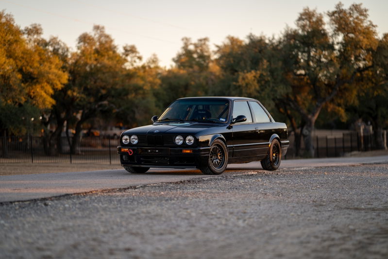 Black 1989 BMW 325is coupe with black rims, tow hook, and aftermarket trim.