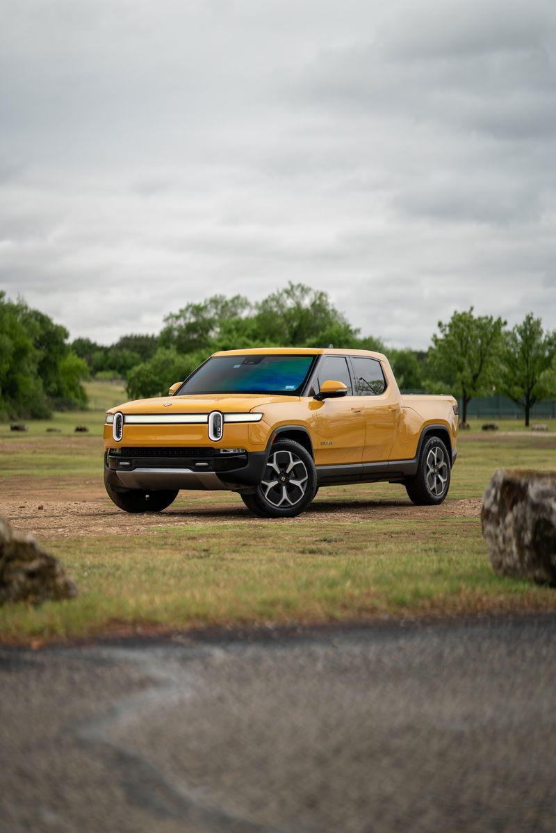 Yellow Rivian R1T pickup truck with black rims and trim parked in a grassy field.