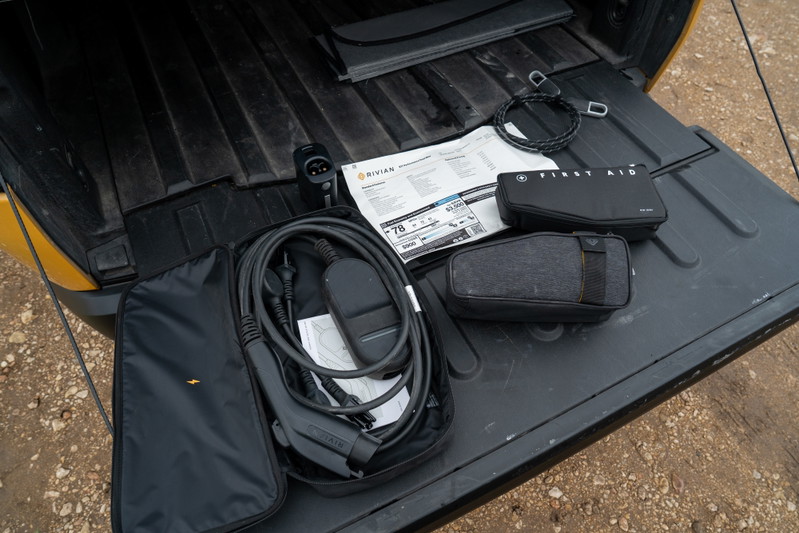 Rivian R1T charging cable and first aid kit in yellow pickup truck bed.