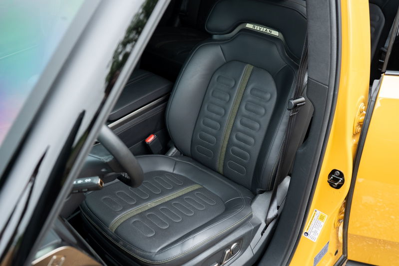 Yellow 2022 Rivian R1T driver's seat with perforated leather, green trim, and Rivian logo.