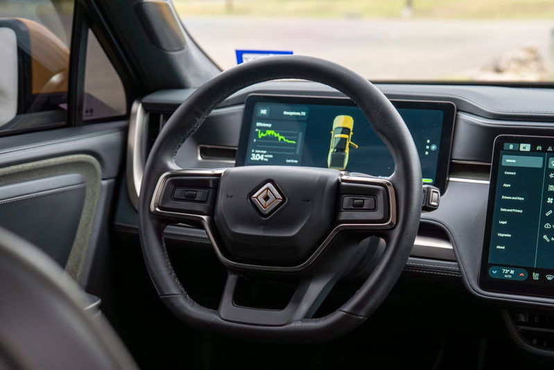 Interior of a yellow Rivian R1T, showing the steering wheel, dashboard, and infotainment screens.