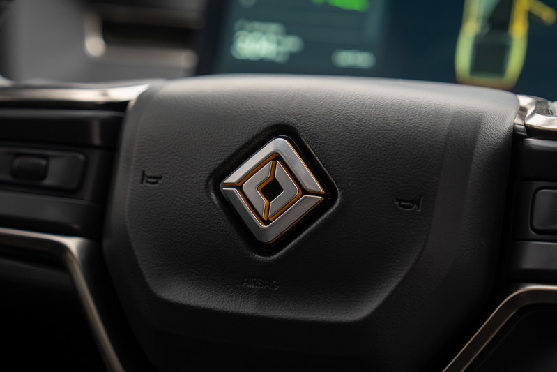 Close-up of the steering wheel in a yellow 2022 Rivian R1T, featuring the illuminated logo.