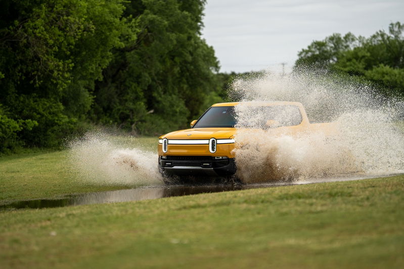 Yellow Rivian R1T pickup truck splashing through water.