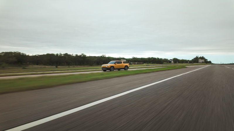 Yellow Rivian R1T driving on a highway with a blur effect.