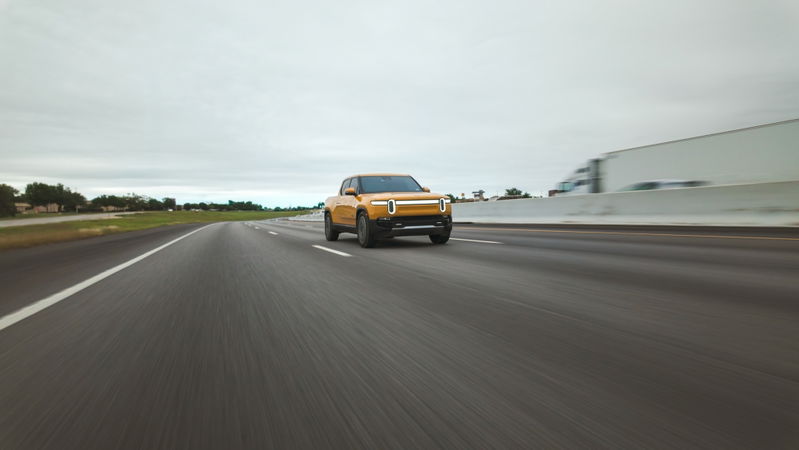 Yellow Rivian R1T electric pickup truck driving on highway with motion blur.