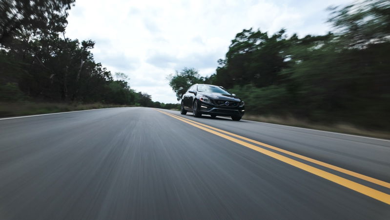 Black 2015 Volvo V60 R-Design Polestar drives on a road with double yellow lines.