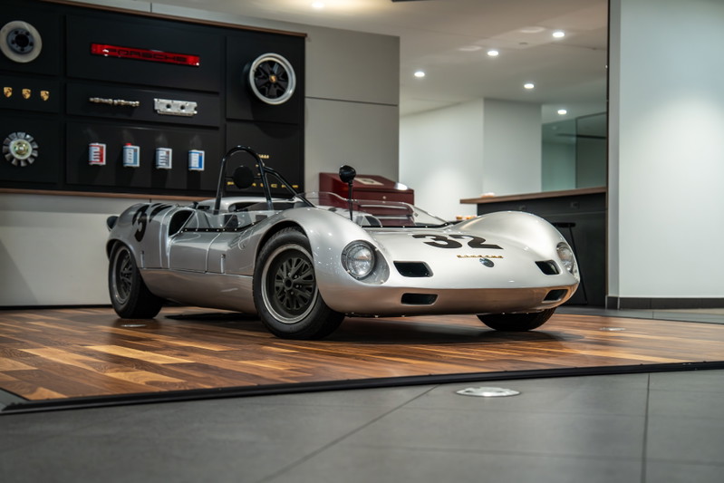 Silver 1964 Elva Porsche 4-Cam race car with black rims and racing livery.