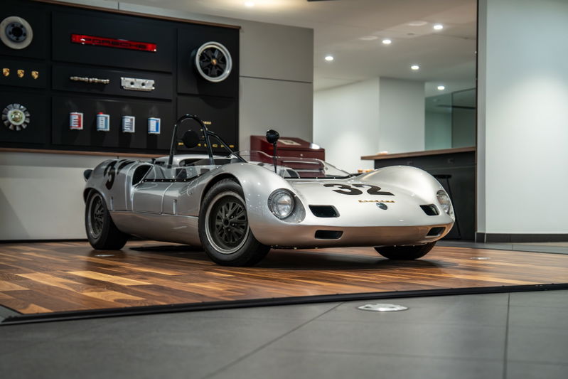 Silver 1964 Elva Porsche 4-Cam race car with black rims and racing livery.