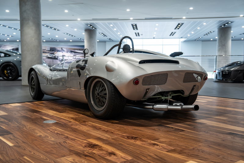 Silver 1964 Elva Porsche 4-Cam race car with black livery on rims and racing number 77.