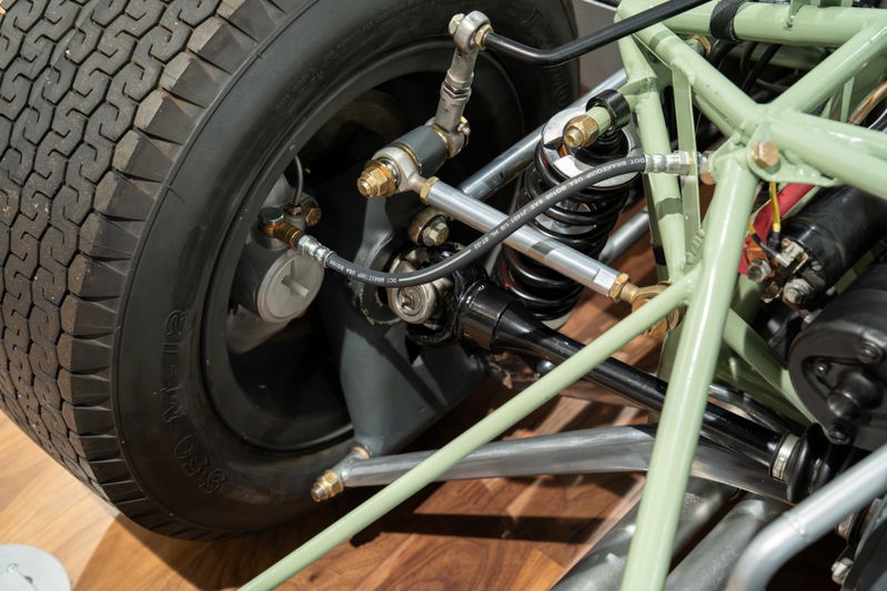 Close-up of a vintage 1964 Elva Porsche 4-cam's black tire, green tubular chassis, and suspension system.