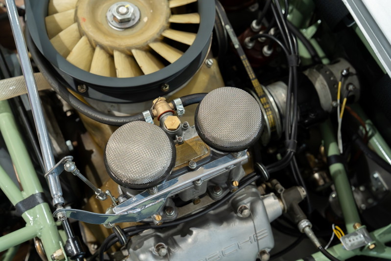 Close-up of a 1964 Elva Porsche 4-cam engine with dual carburetors and cooling fan.