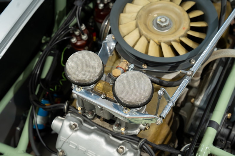 Close-up of a 1964 Elva Porsche 4-Cam engine, featuring dual carburetors with mesh air filters and cooling fan.