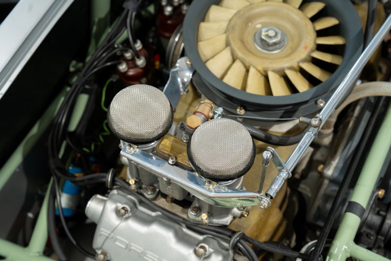 Close-up of a 1964 Elva Porsche 4-Cam engine, featuring dual carburetors with mesh air filters and cooling fan.