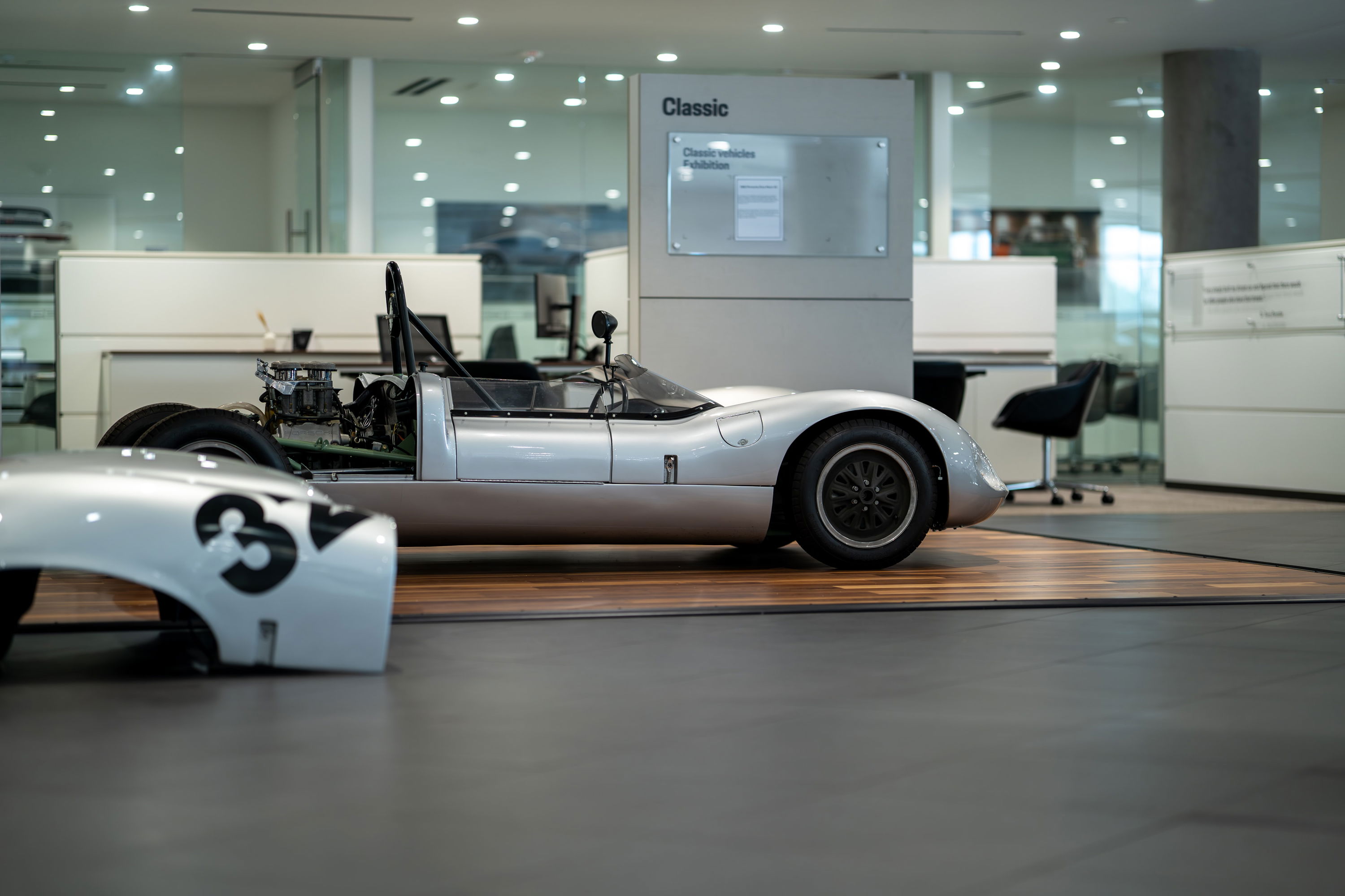 1964 Elva Porsche 4 Cam racer in silver, exposed engine, black rims, minimalist livery.