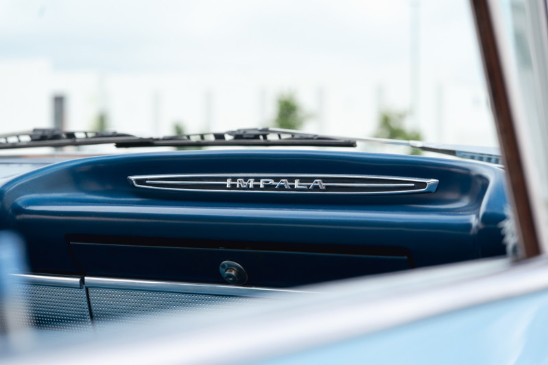 Close-up of a blue 1963 Chevrolet Impala's dashboard with "IMPALA" chrome trim.