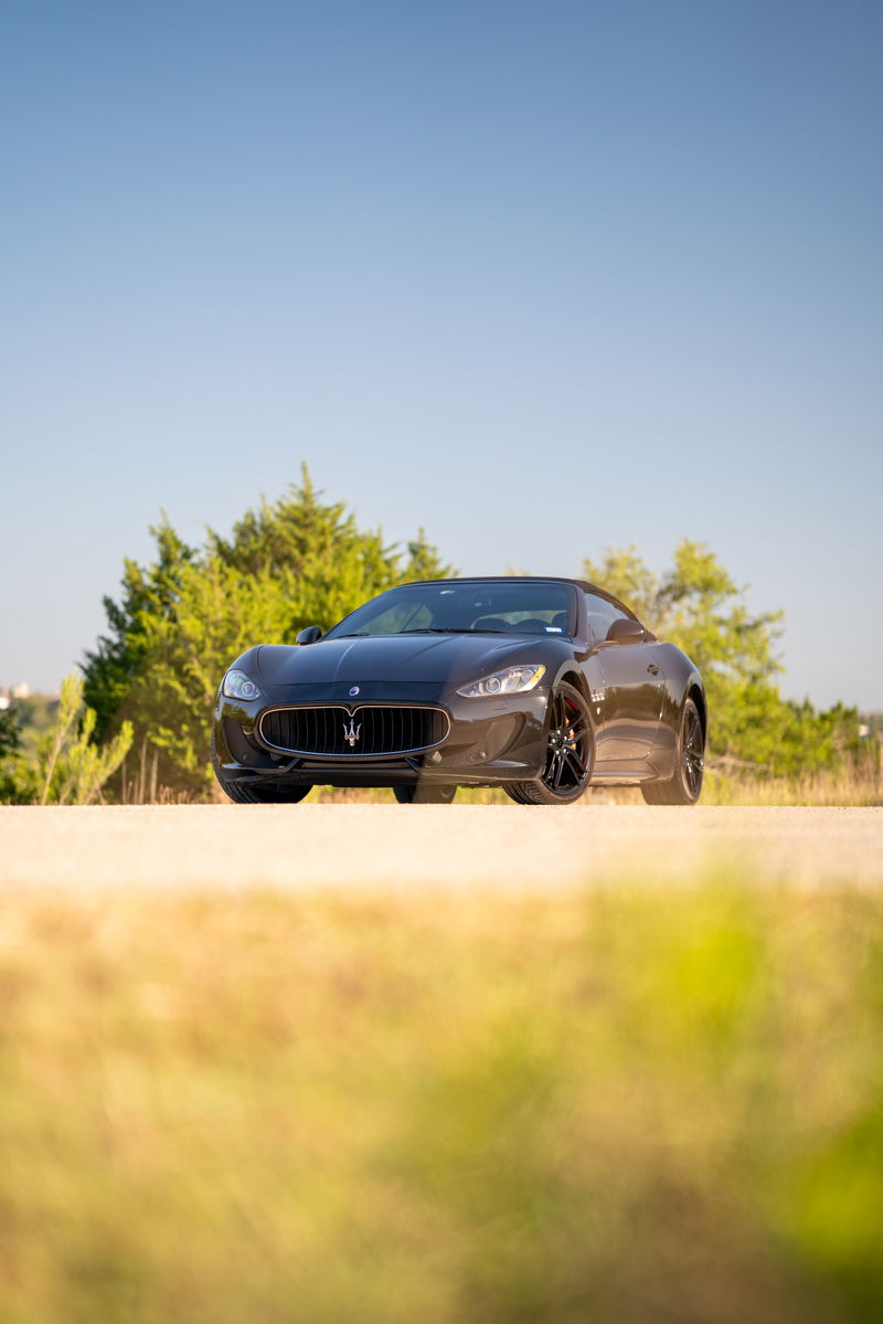 Front view of a dark gray 2016 Maserati GranTurismo convertible with black rims and red brake calipers.