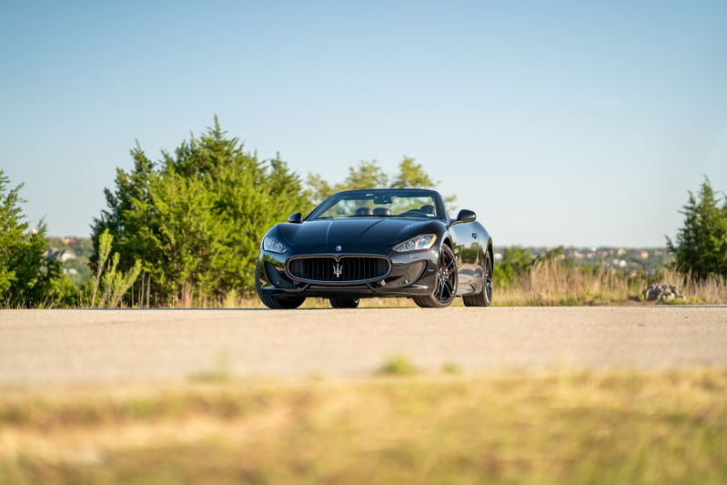 Black 2016 Maserati GranTurismo convertible with dark rims parked on a road.