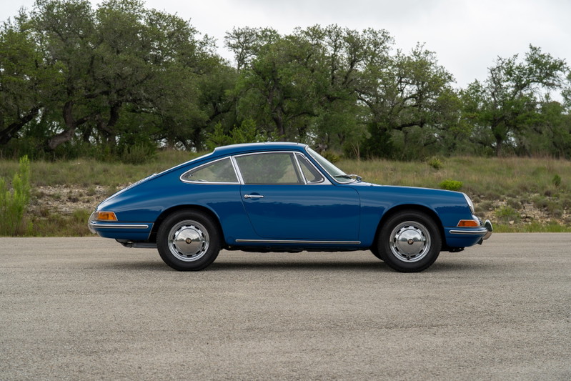 Blue 1965 Porsche 912 coupe with chrome hubcap rims parked on asphalt.