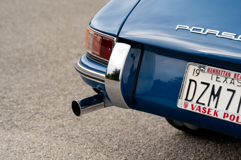 Detail of a vintage blue Porsche 912's rear bumper, exhaust pipe, and chrome trim.
