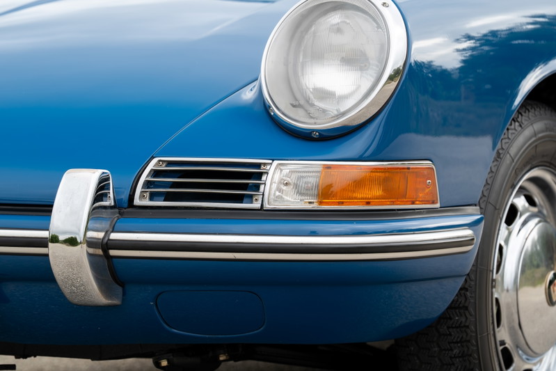 Close-up of a blue 1965 Porsche 912's front bumper, headlight, and chrome trim.
