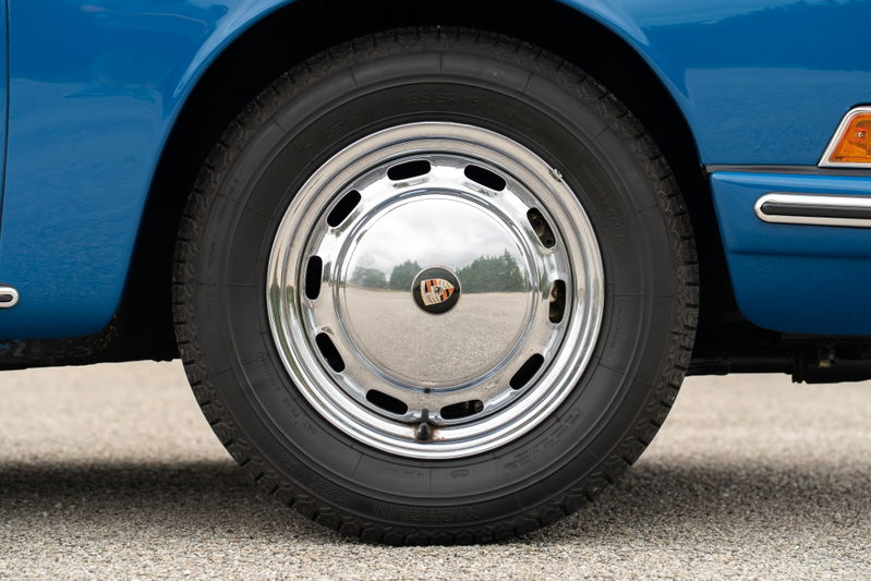 Close up of a blue 1965 Porsche 912 wheel with chrome hubcap and Michelin tire.