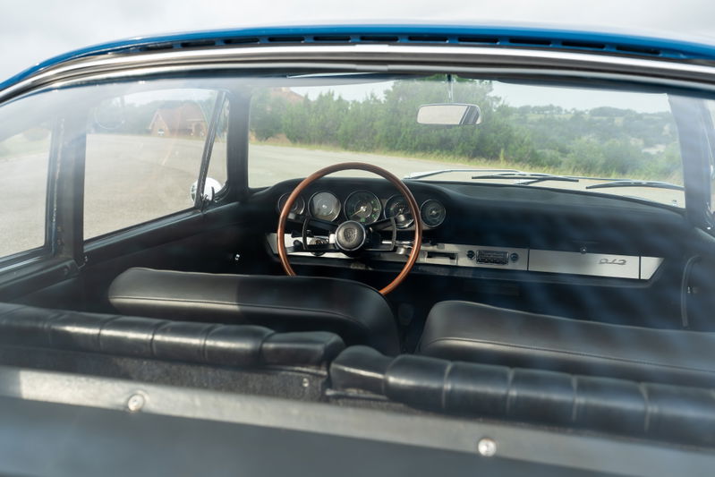 Interior of a blue 1965 Porsche 912, showing black leather seats, a wood-rimmed steering wheel, and silver dash trim.