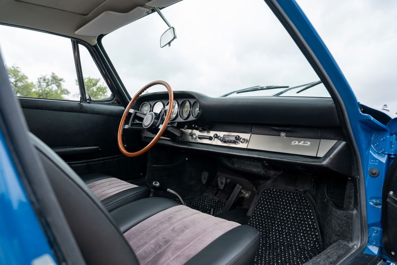 Interior of a blue 1965 Porsche 912, featuring a wood-rimmed steering wheel and 912 badge.