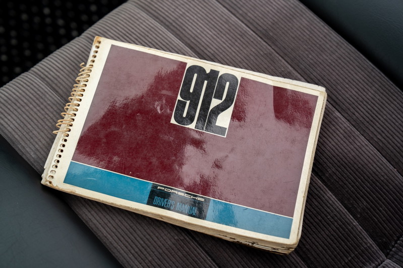 Vintage Porsche 912 driver's manual sits on corduroy seat.