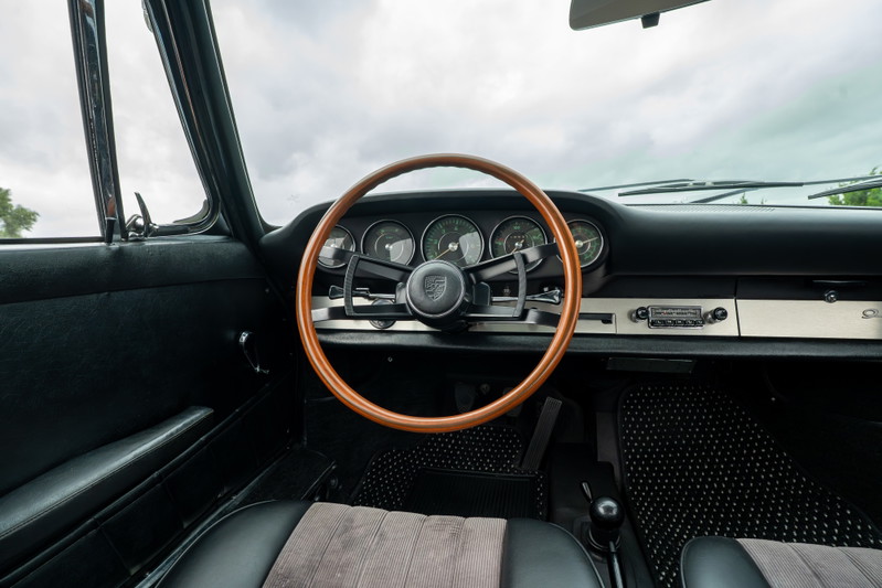 Vintage blue Porsche 912 interior with wood-rimmed steering wheel, classic gauges, and AM/FM radio.