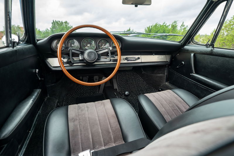 Interior of a 1965 Porsche 912 coupe with a wooden steering wheel and black seats.