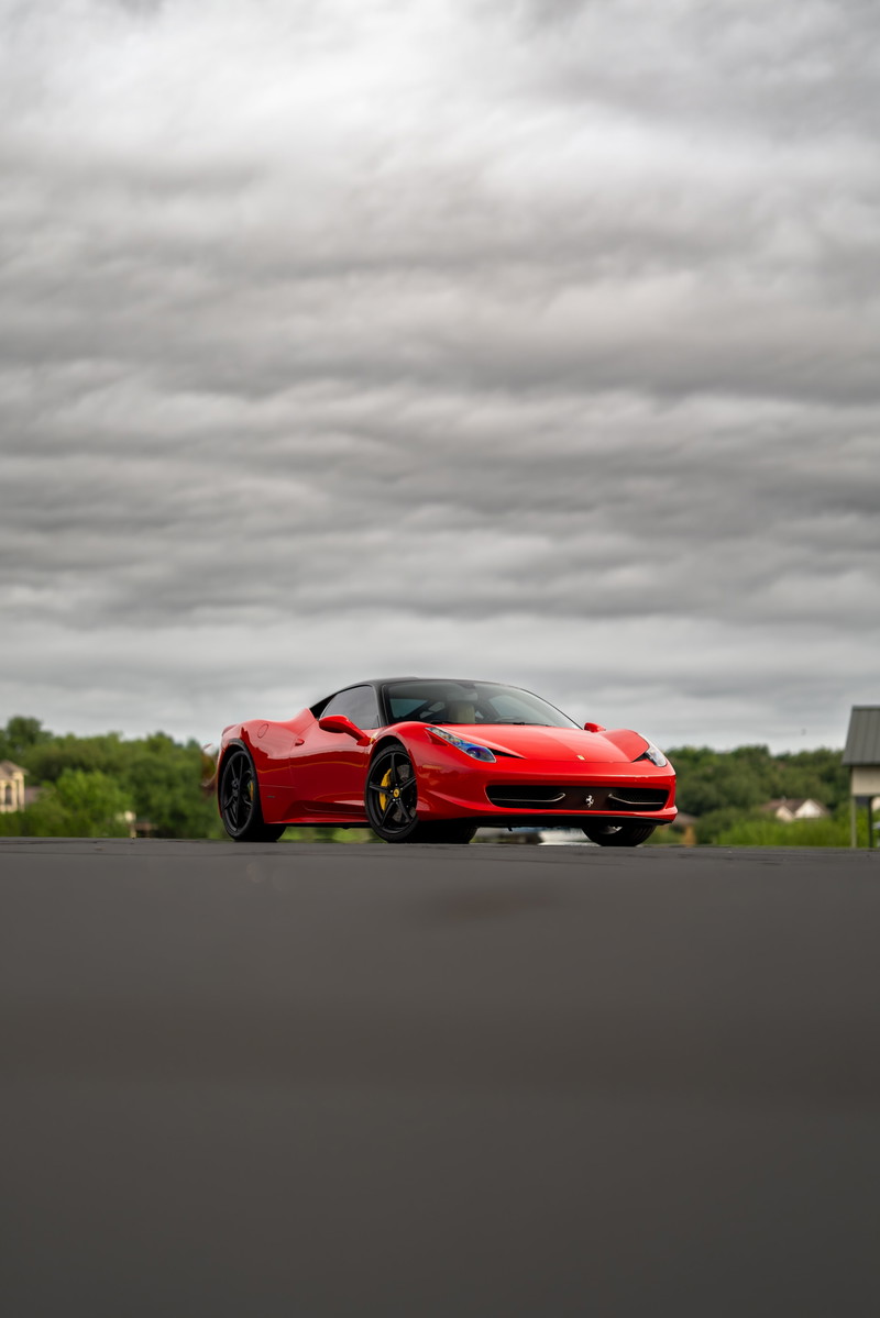Red Ferrari 458 Italia with black rims and yellow brake calipers, parked under a cloudy sky.