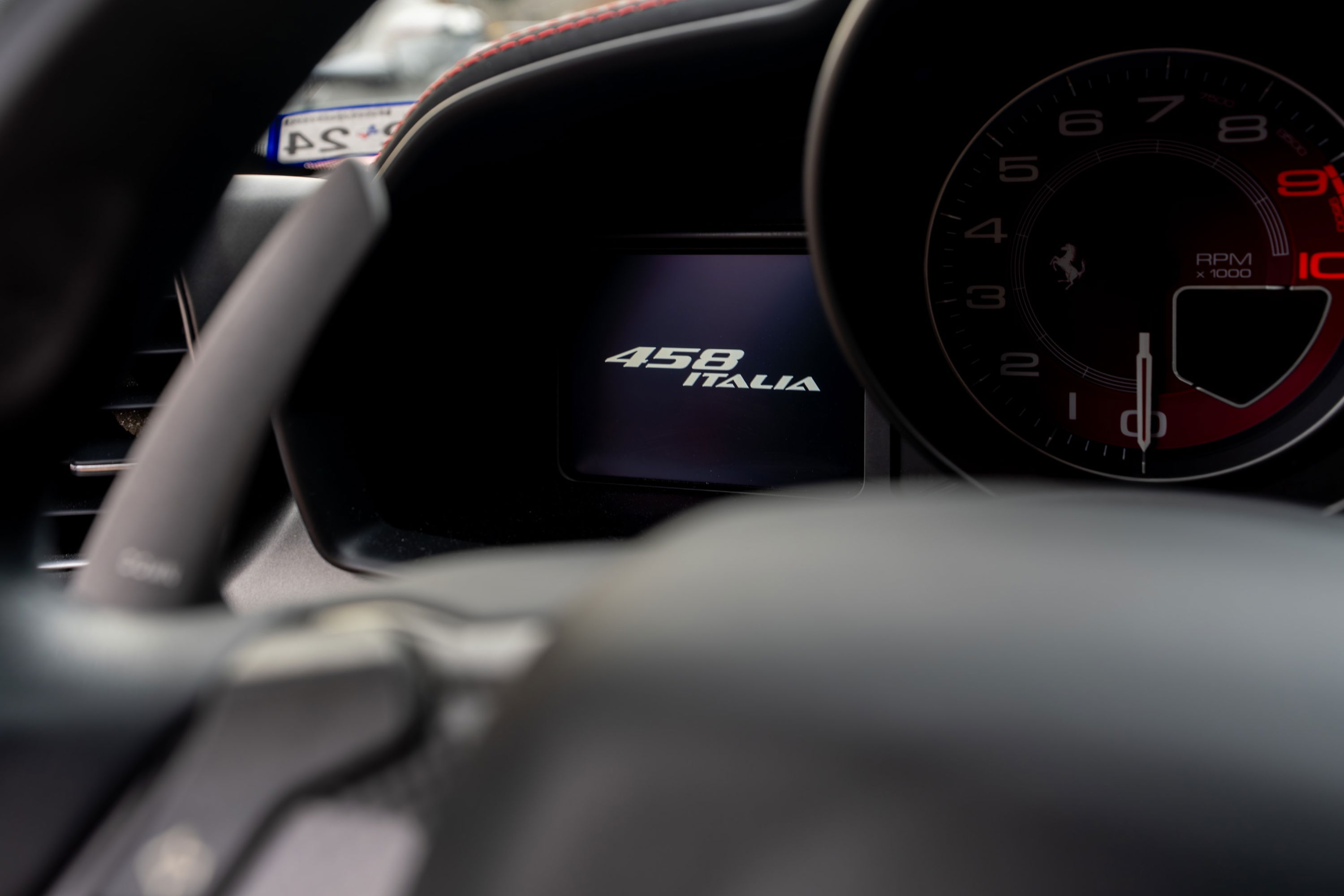 Interior shot of a Ferrari 458 Italia showing the digital display with "458 ITALIA" and the tachometer.