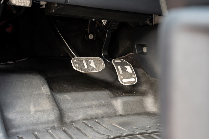 Close-up of the clutch and brake pedals in a red 2022 Ford F-150 Roush, featuring custom R-branded pedal covers.