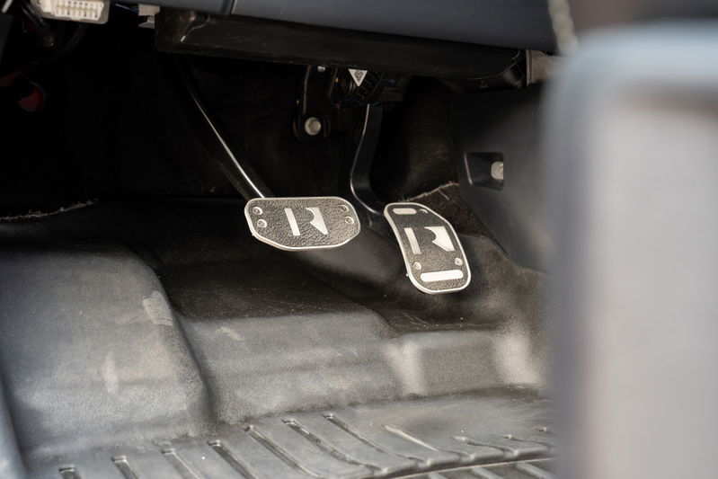 Close-up of the clutch and brake pedals in a red 2022 Ford F-150 Roush, featuring custom R-branded pedal covers.