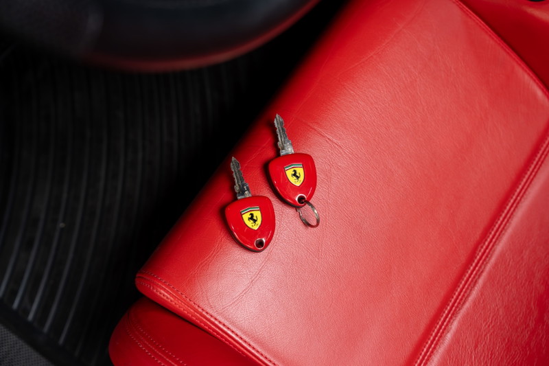 Two red Ferrari Enzo keys with prancing horse logo on red leather seat.
