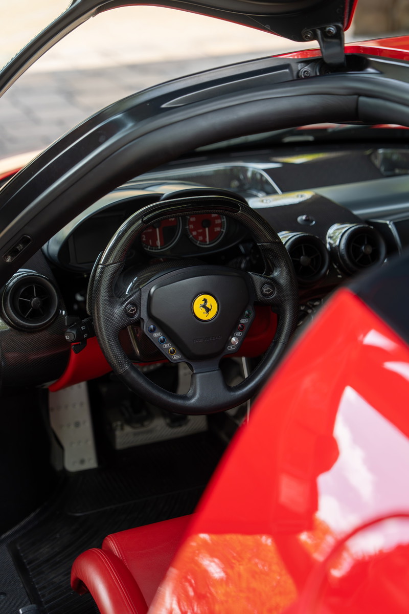 Rosso Corsa Ferrari Enzo interior with carbon fiber steering wheel and red leather seats.