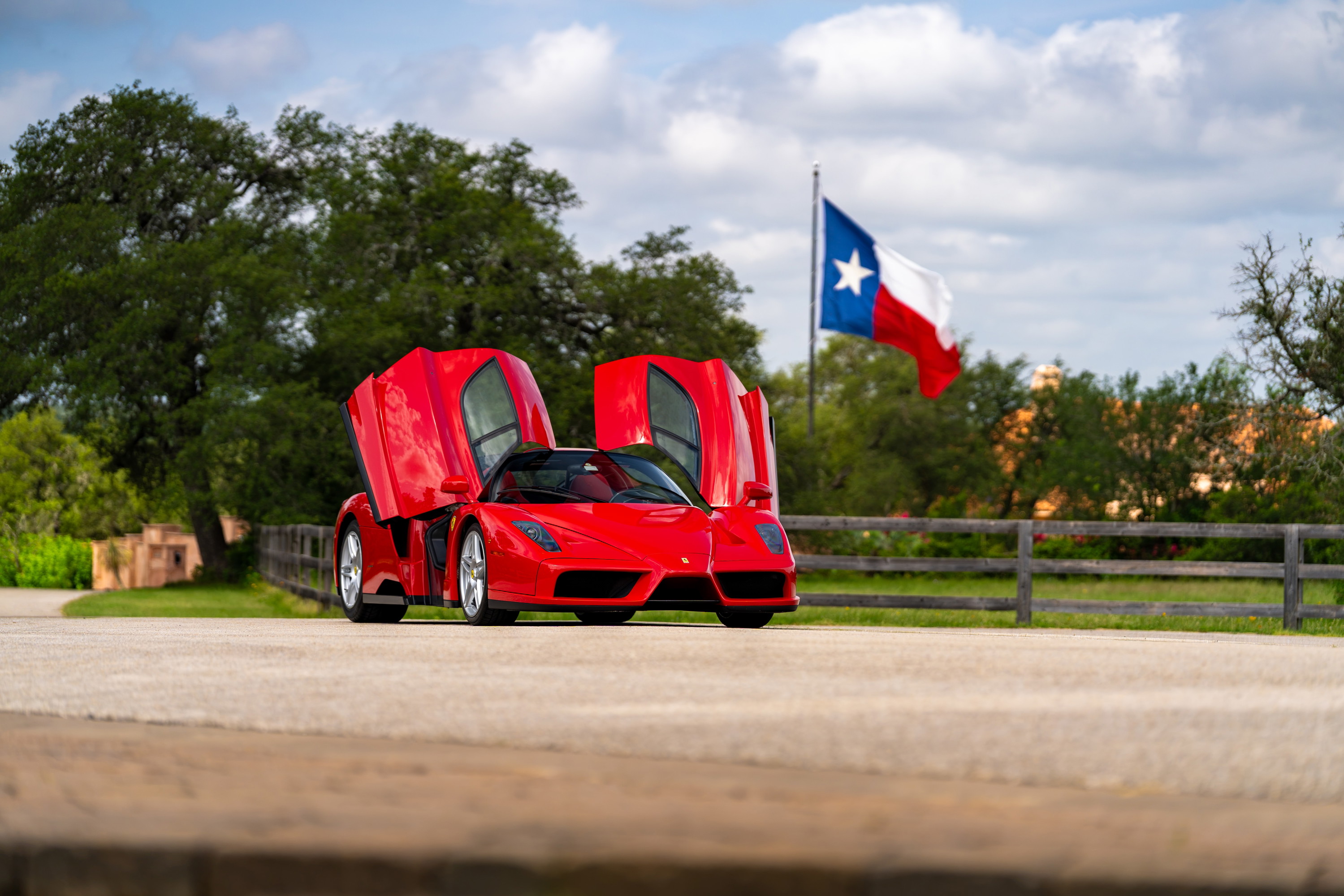 Red 2003 Ferrari Enzo with dihedral doors open and silver rims, Texas flag in background.
