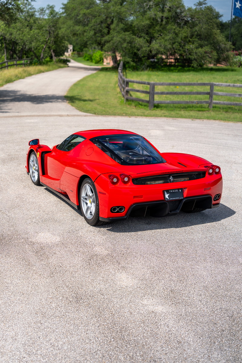 Rear view of a red 2003 Ferrari Enzo with silver rims and dual exhaust pipes.