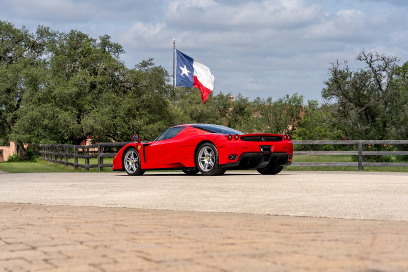 Red 2003 Ferrari Enzo with silver rims, parked outdoors near a Texas flag.
