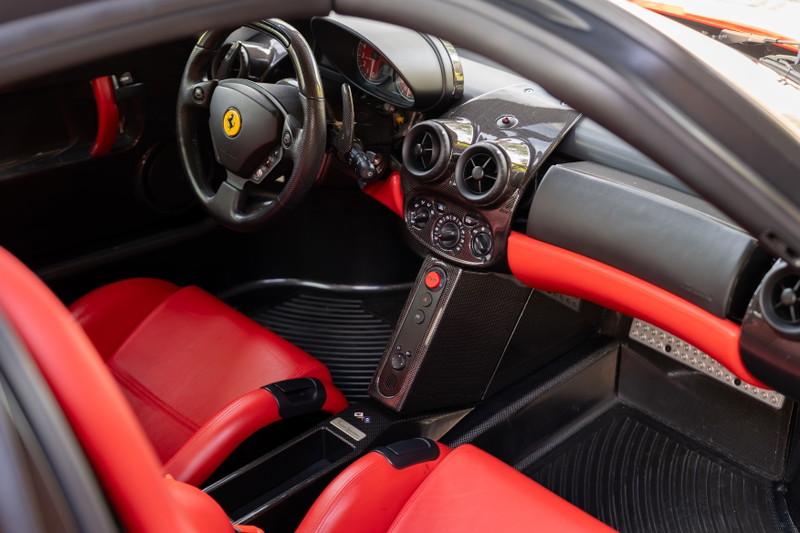 Interior view of a red 2003 Ferrari Enzo, featuring red leather seats and carbon fiber trim.
