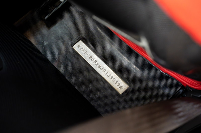 Ferrari Enzo VIN plate, with part of the carbon fiber trim and red interior visible.