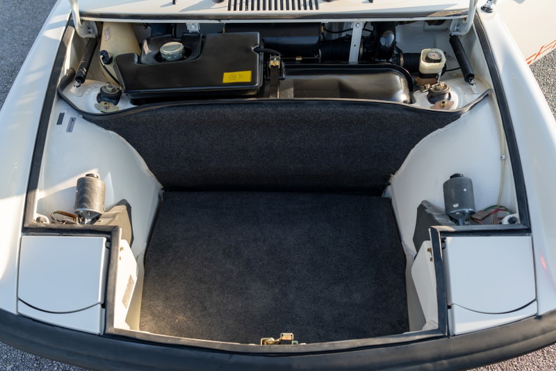 Front trunk of a white 1974 Porsche 914 Can-Am LE, showing carpeted storage and spare tire well.