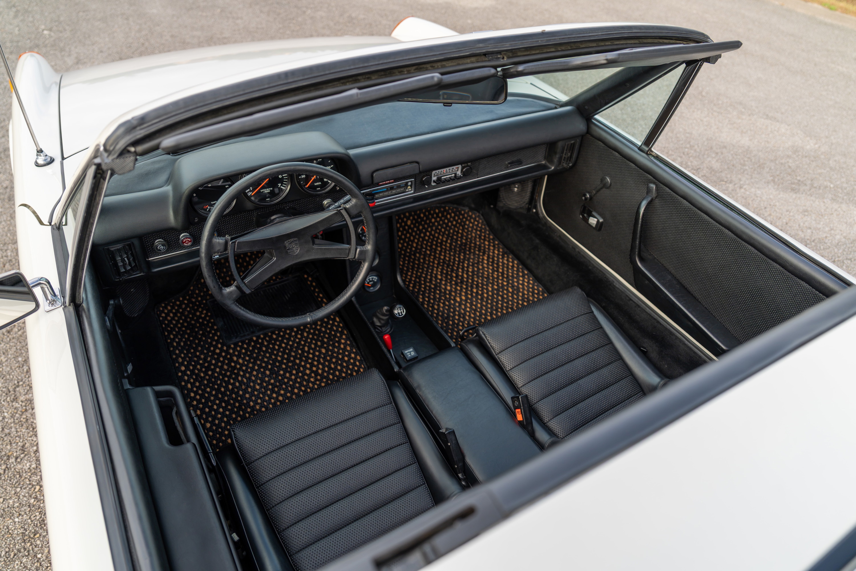 Interior of a white 1974 Porsche 914 Can-Am with black seats and tan floor mats.