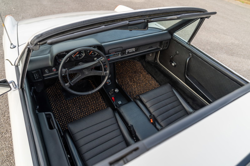 Interior of a white 1974 Porsche 914 Can-Am with black seats and tan floor mats.